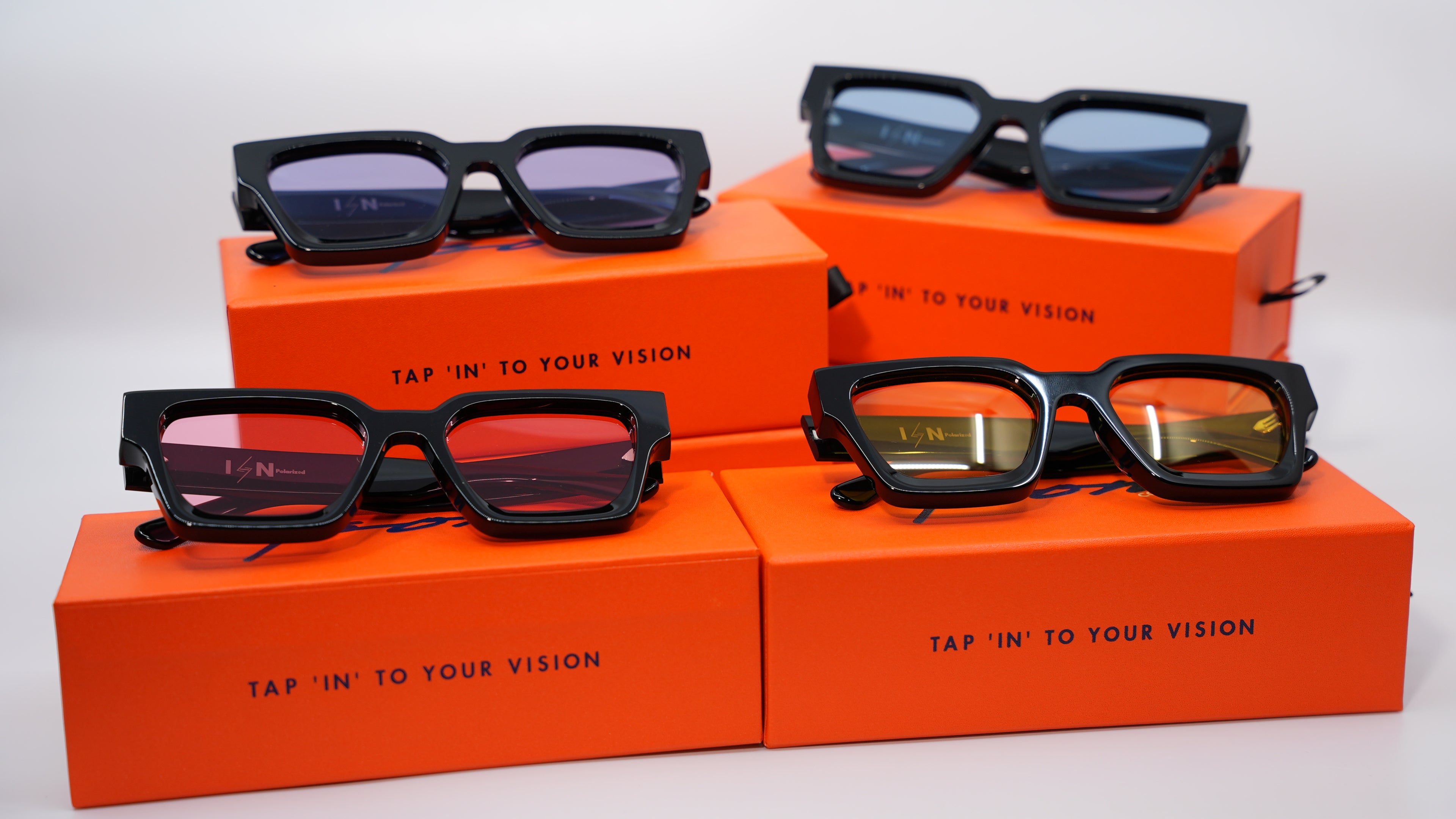 Black sunglasses on orange boxes with 'Tap In' to Your Vision' text on a white background