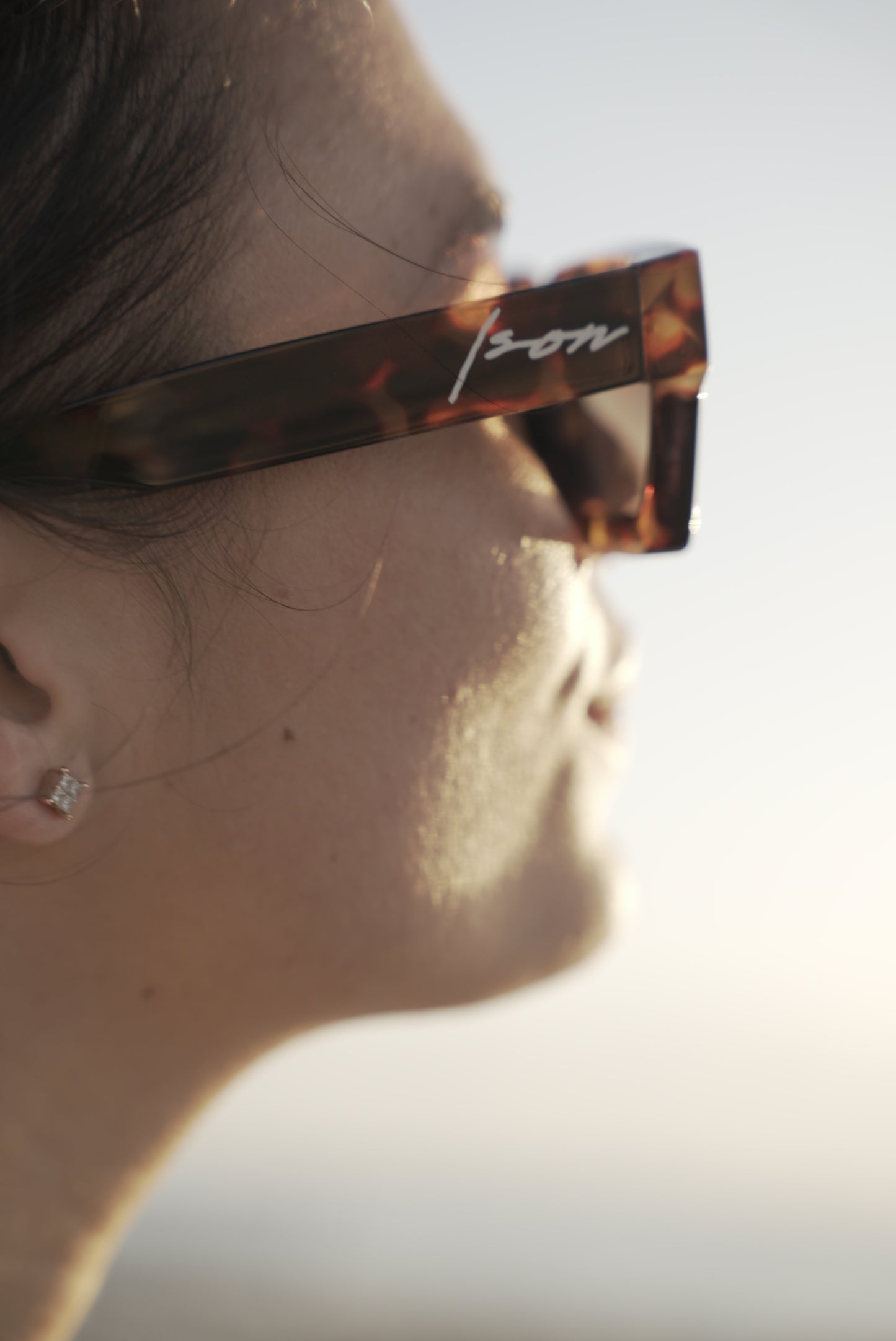 A side profile of a women wearing ison couture square-shaped tortoise shell sunglasses with gradient lenses staring at sun.