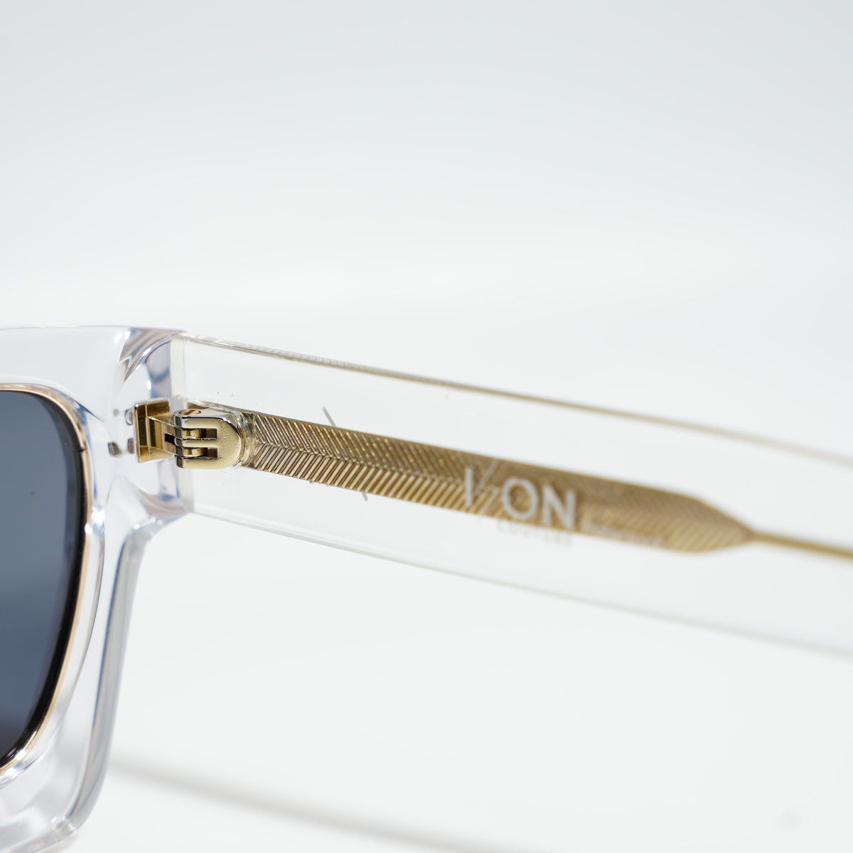 Close-up of the engraved gold metal core rod and gold hinge inside the crystal clear acetate temple
