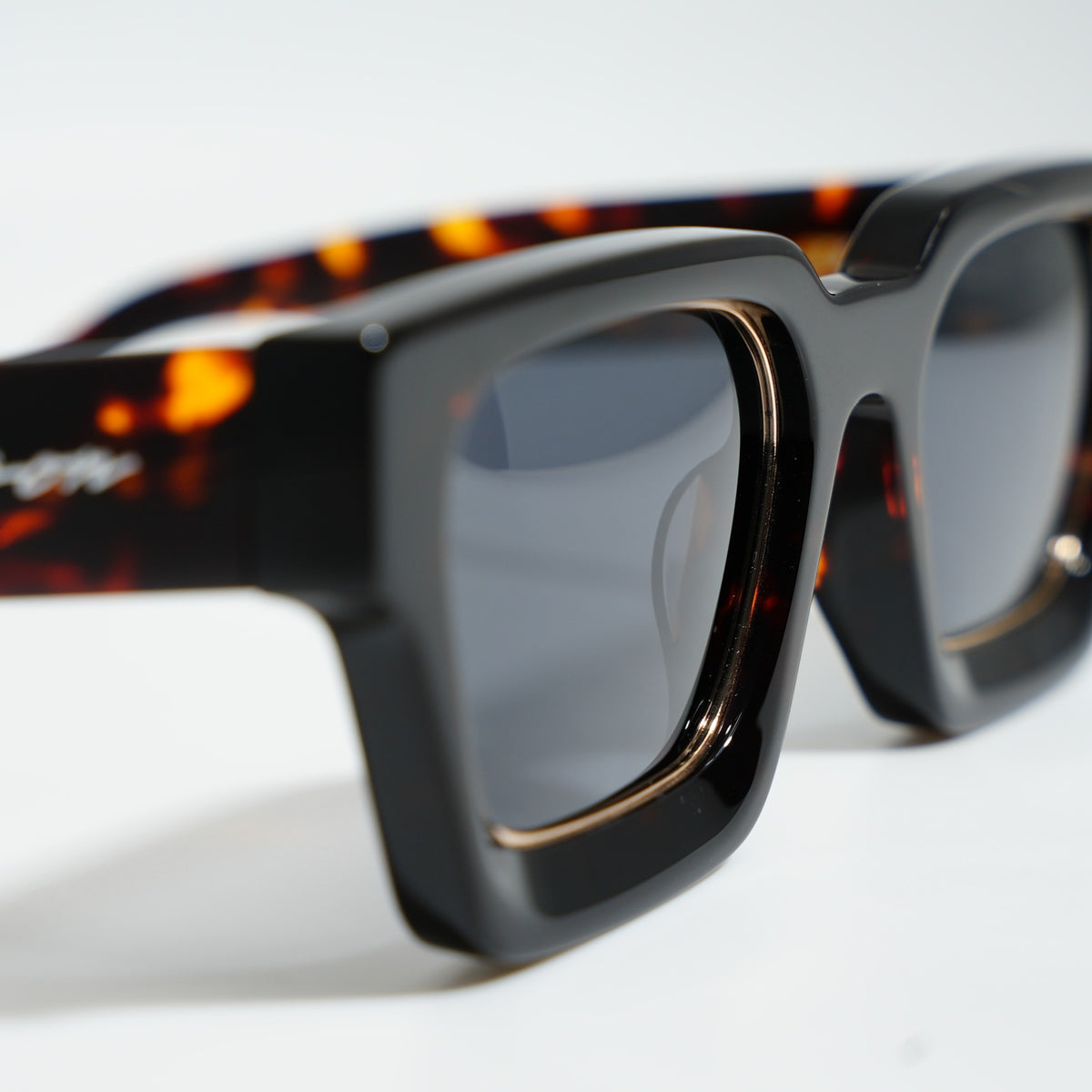 Close-up of Dark Tortoise frame showing amber tortoise flecks on the temple, Ison signature, and gold lens rim