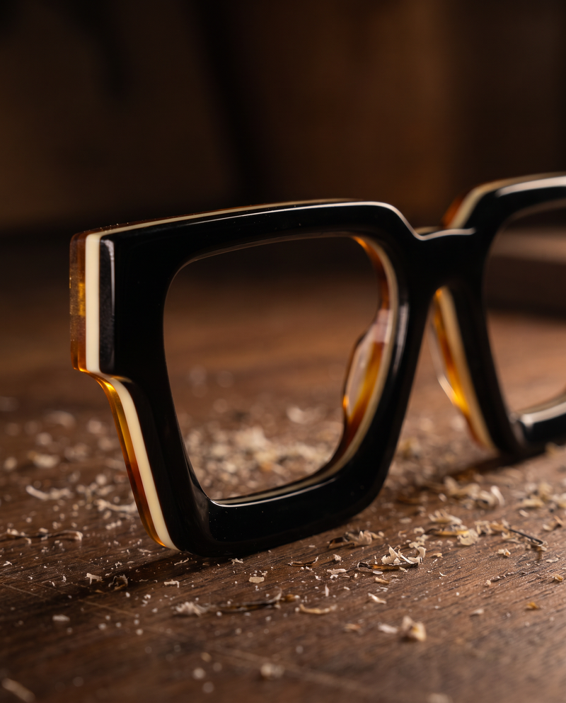 Square sunglasses frame cut from layered acetate, showing black, ivory and amber layers along the edge