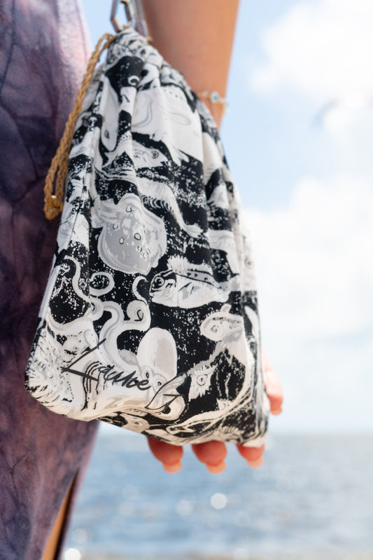Drawstring bag with black and white pattern held by a person against a blurred natural background