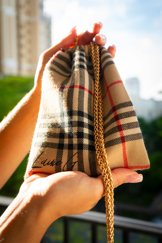 Burberry style handbag with gold chain held by a person outdoors